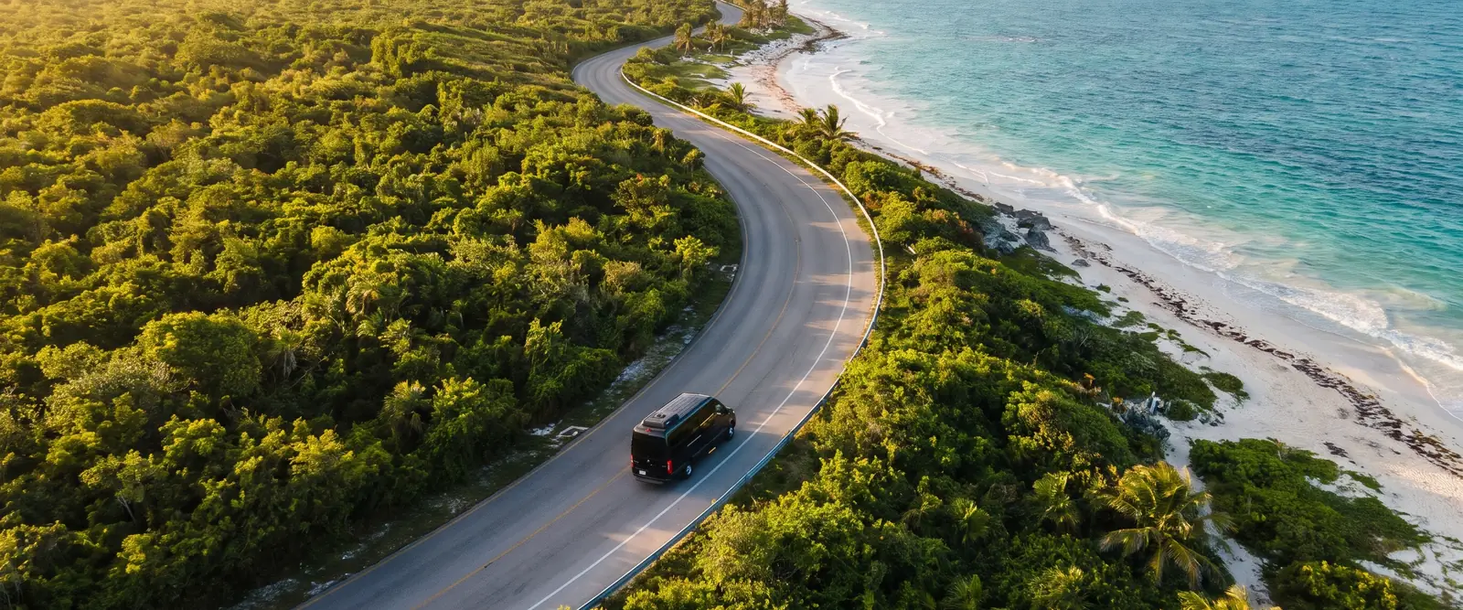 Van negra en una carretera costera entre selva y mar en la Riviera Maya